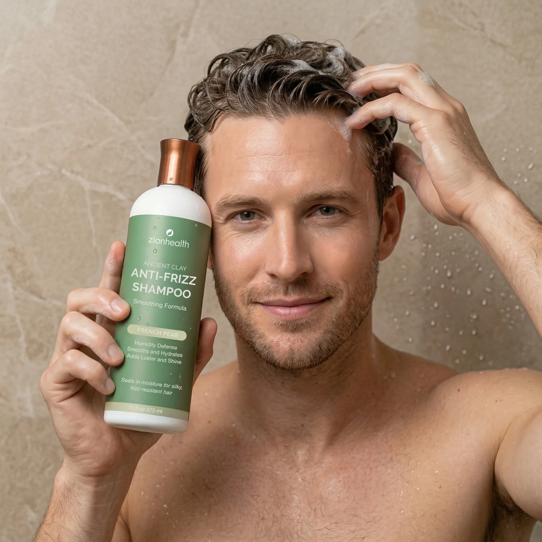 A man in the shower applying Zion Health Ancient Clay Anti-Frizz Shampoo while holding the bottle next to his face with wet hair and foam.